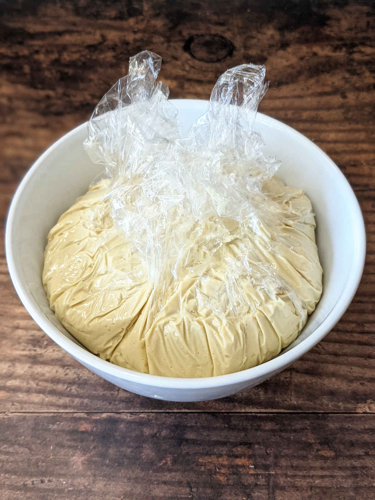 Vegan cheese ball in a bowl wrapped with plastic wrap.