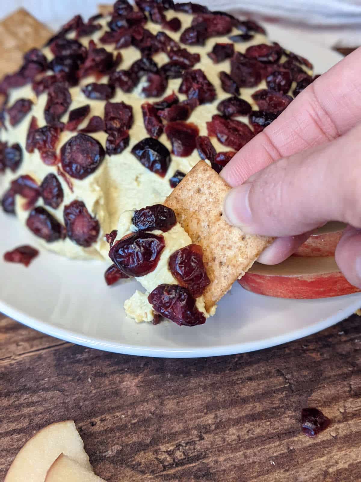 Hand holding cracker to scoop a bite of the vegan cheese ball.