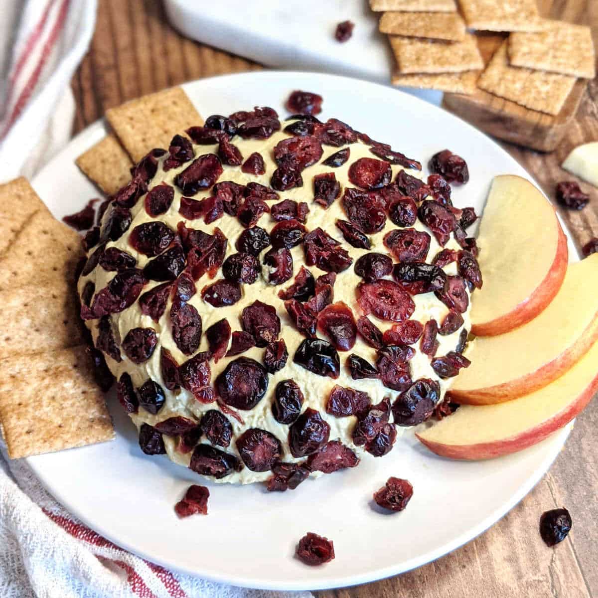 Cranberry vegan cheese ball on platter with crackers and sliced apples.
