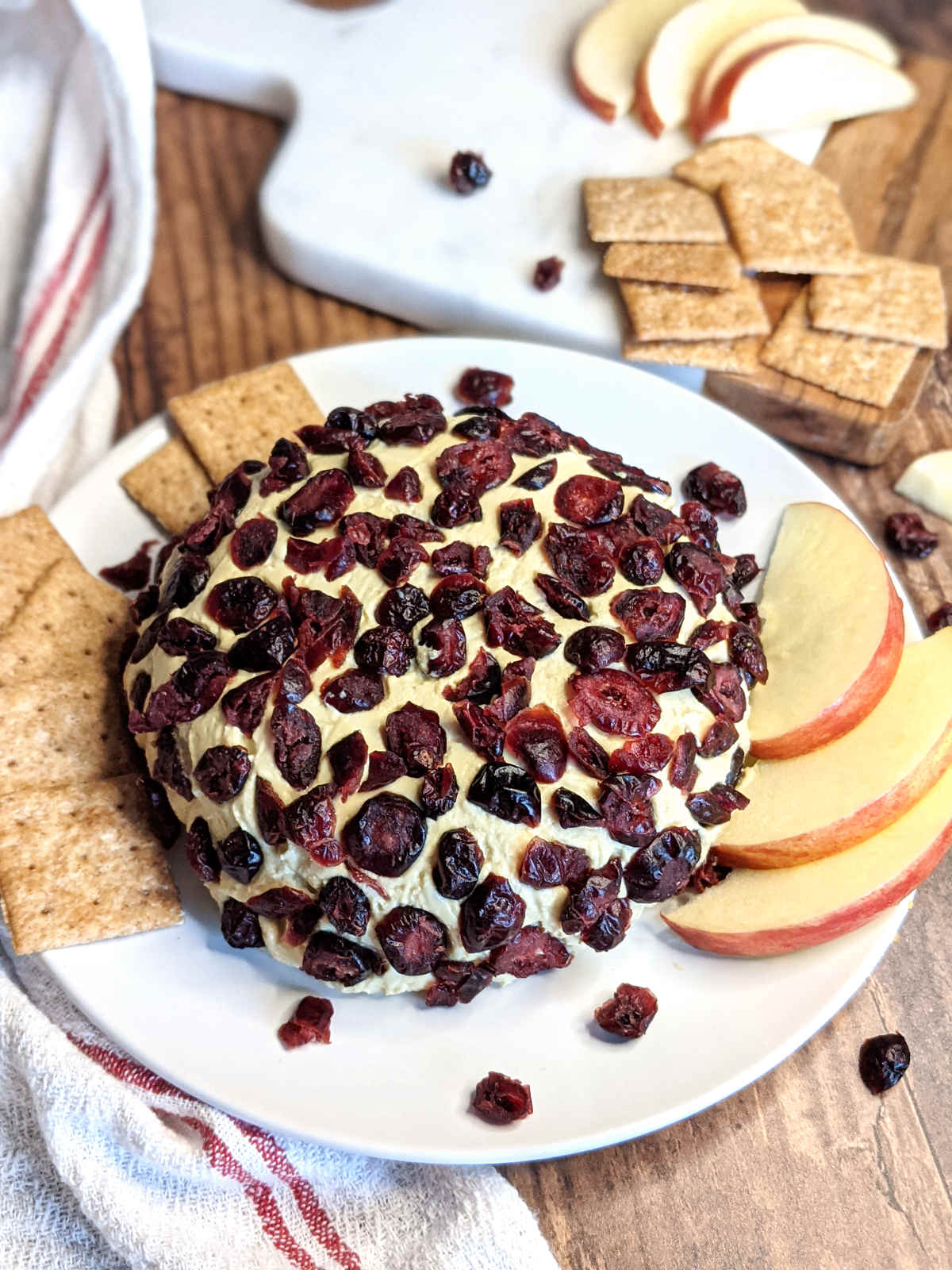 Cranberry vegan cheese ball on platter with crackers and sliced apples.
