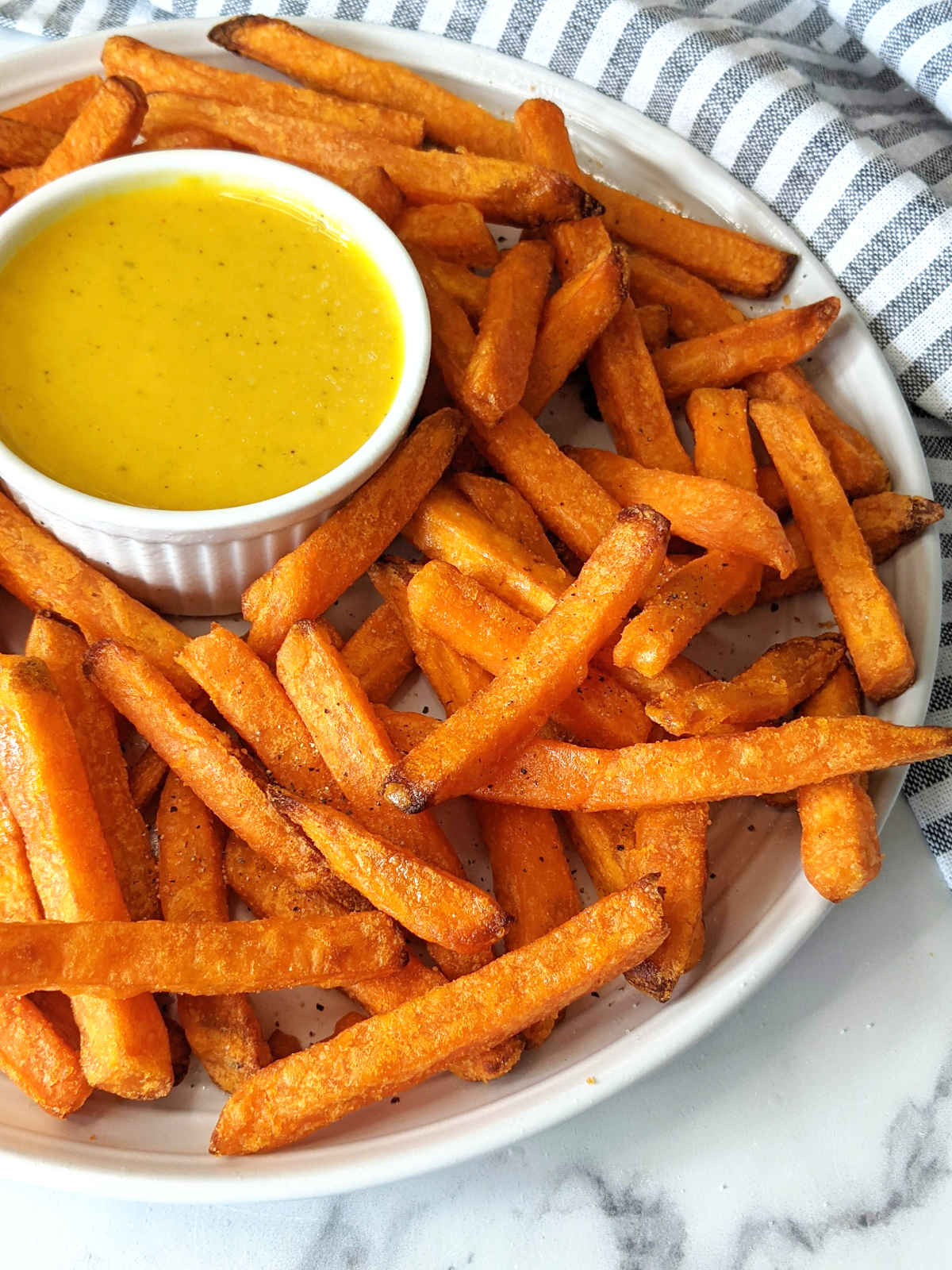 Sweet potato fries on a serving plate with a small bowl of honey mustard.