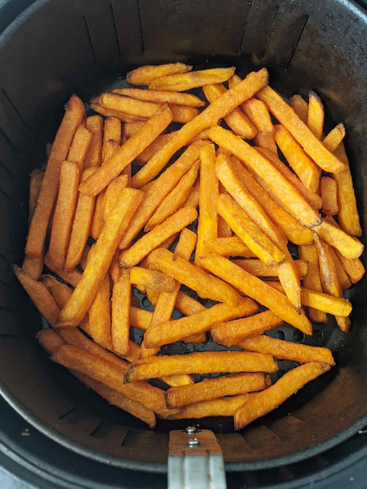 Cooked sweet potato fries in air fryer basket.