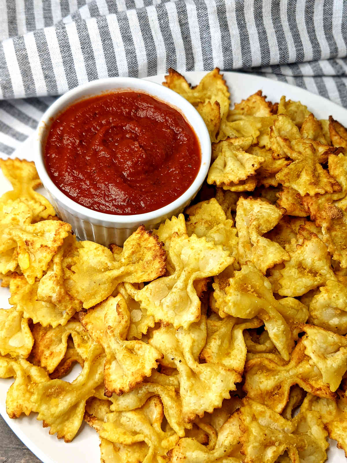 Pasta chips on a plate with a cup of marinara sauce.