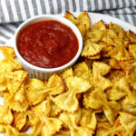 Pasta chips on a plate with a cup of marinara sauce.