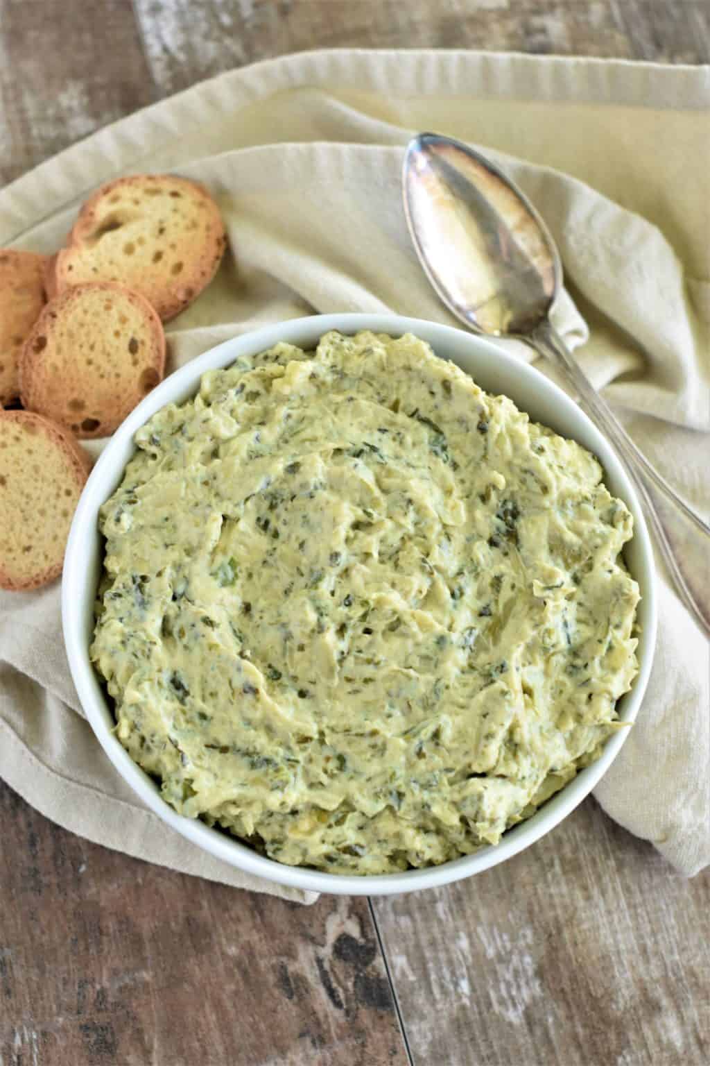 Bowl of the spinach artichoke dip with slices of bread and spoon next to it.