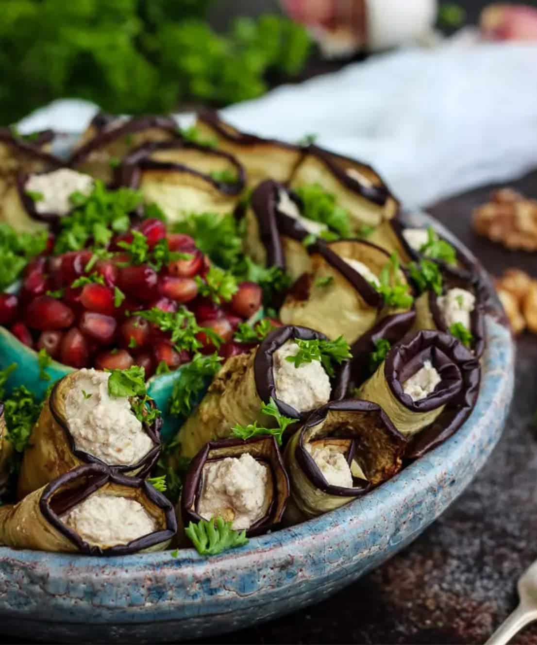 Eggplant wraps on a serving platter with pomegranate seeds in the center.