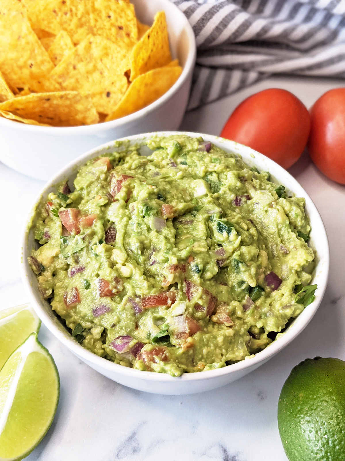 Vegan guacamole in a bowl served with chips and lime slices.
