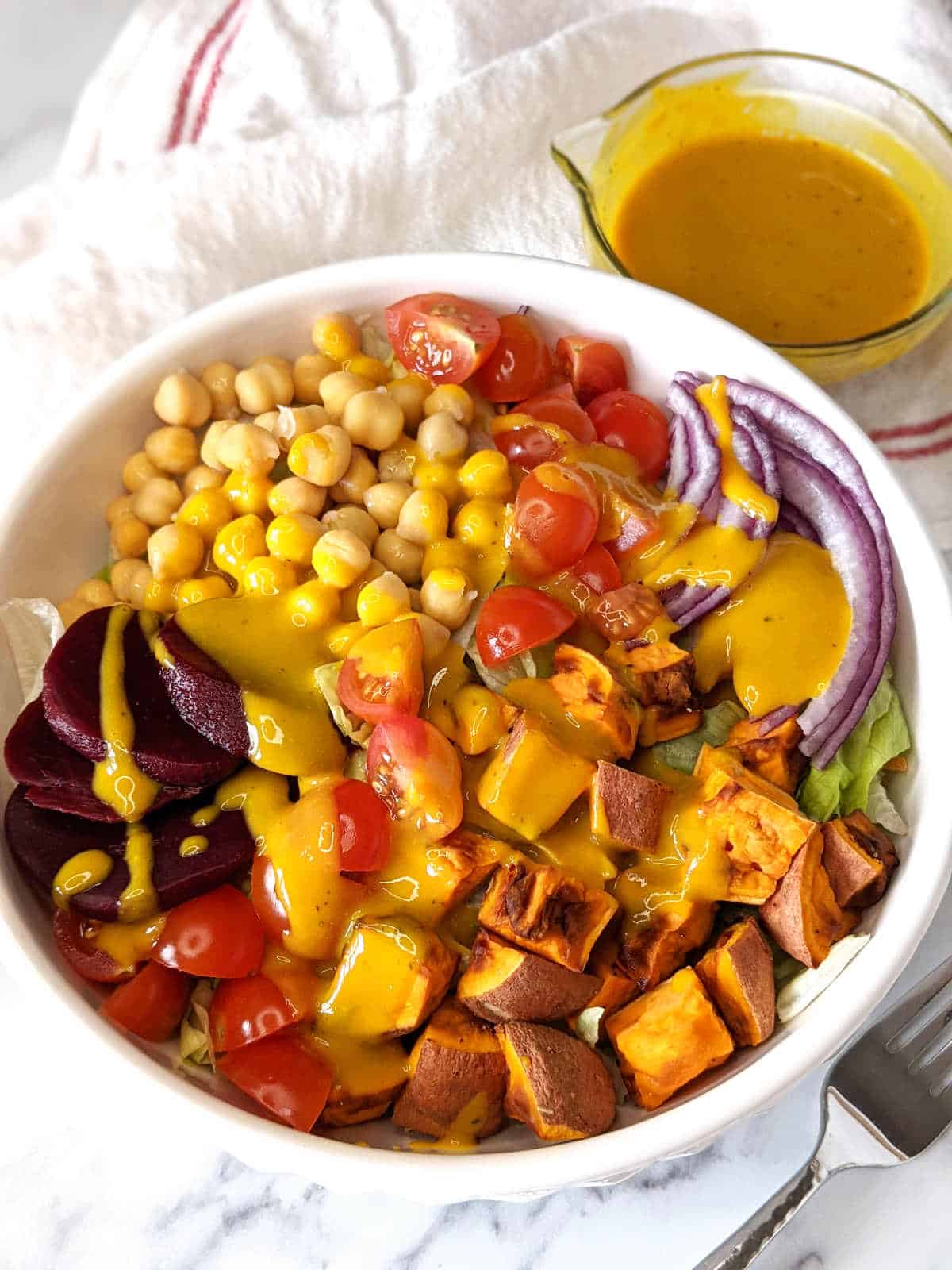 Vegan honey mustard on top of a salad with extra honey mustard in small dish next to salad bowl.