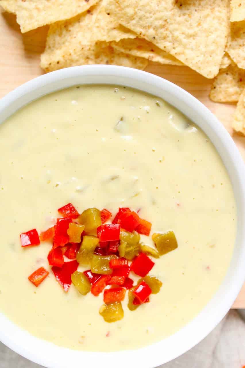 Vegan queso in a bowl topped with peppers and served with tortilla chips.