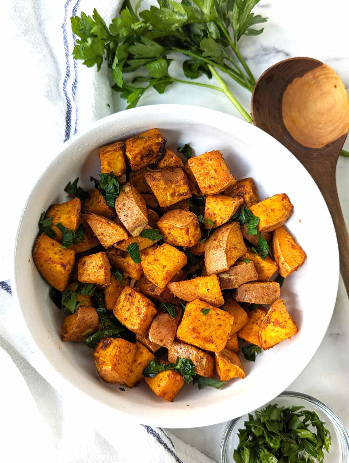 A bowl of air fryer sweet potato cubes tossed with chopped parsley.