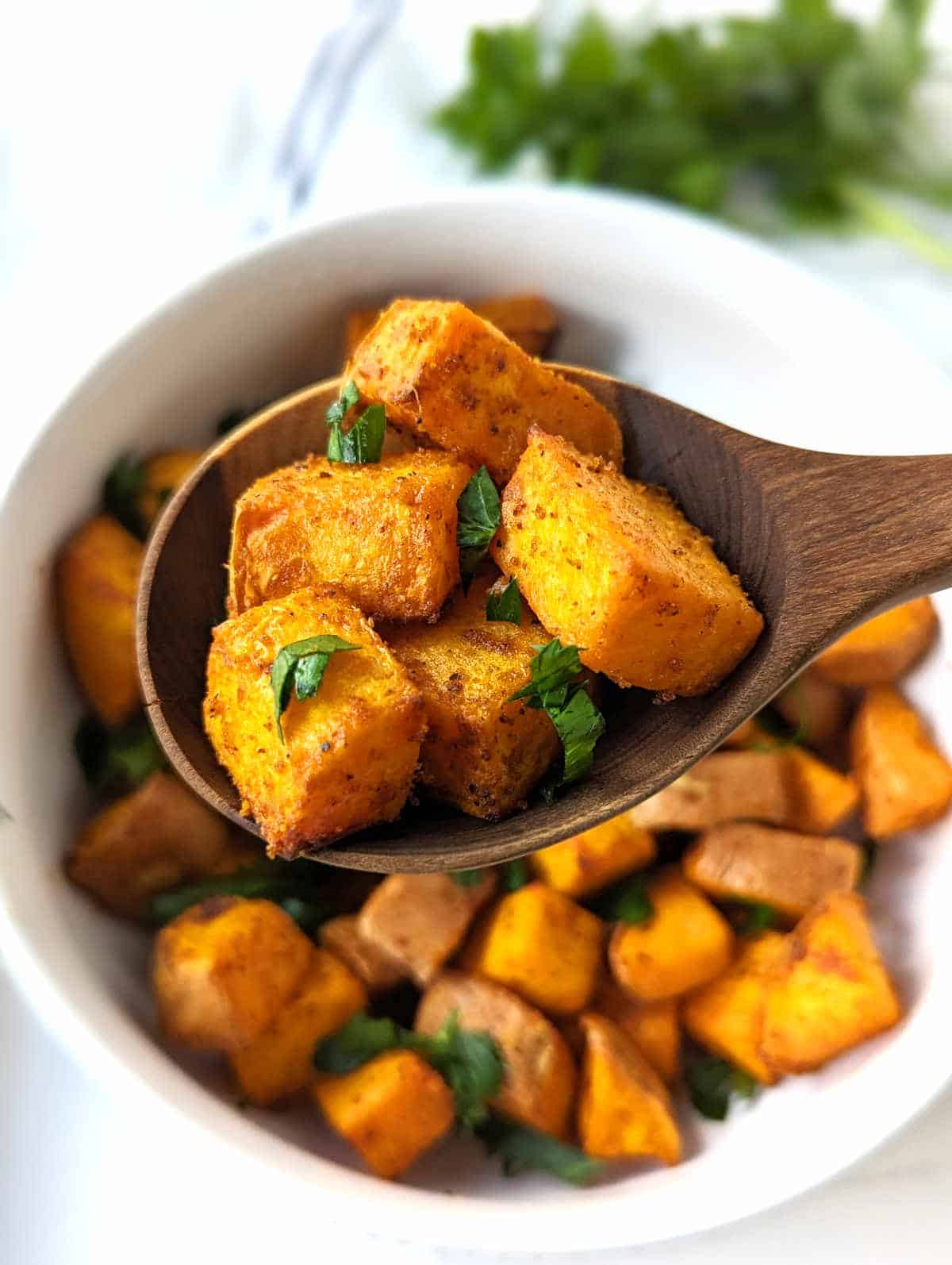 A wooden spoon holding roasted sweet potato cubes.