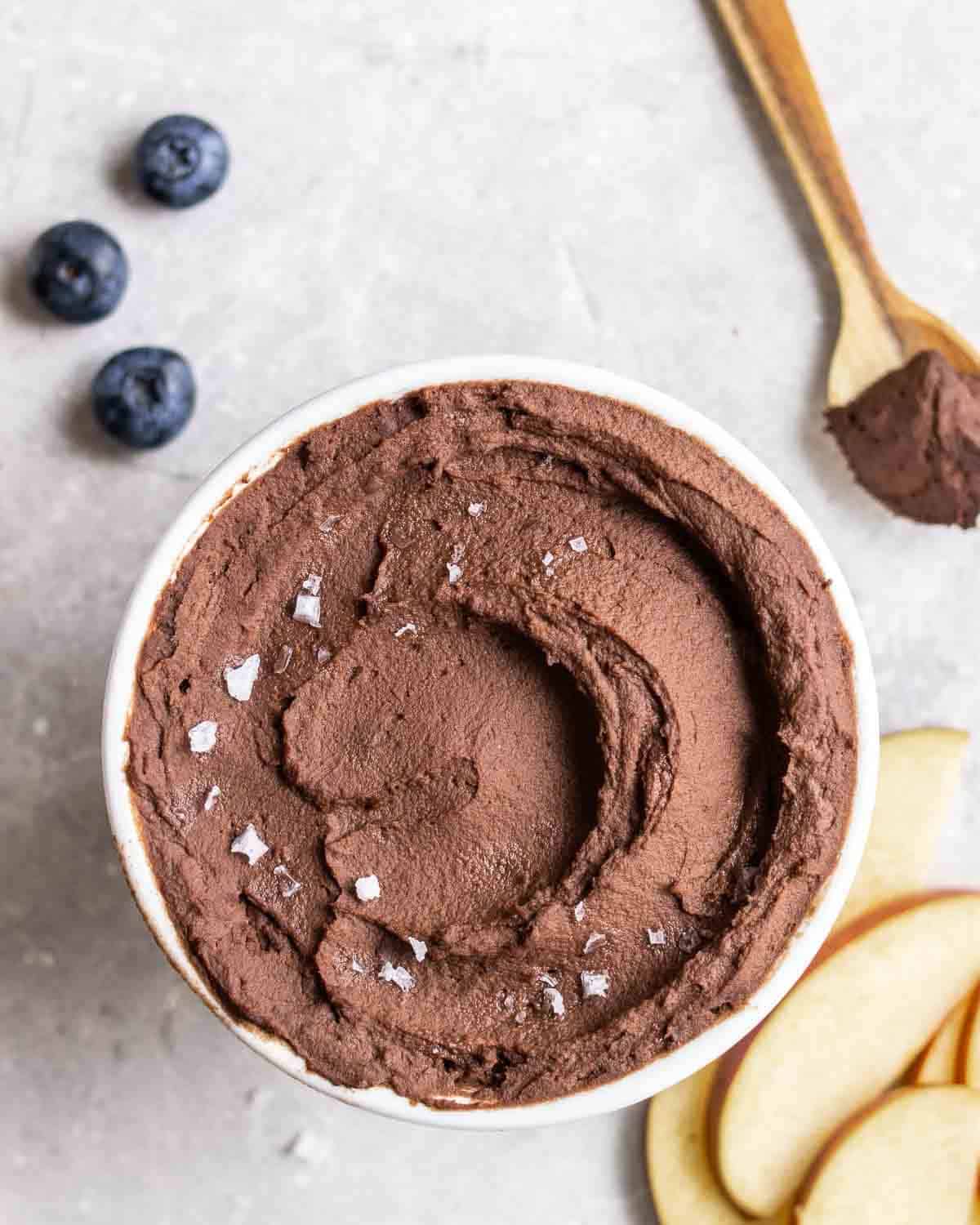Chocolate hummus in a bowl with sliced apple and blueberries.