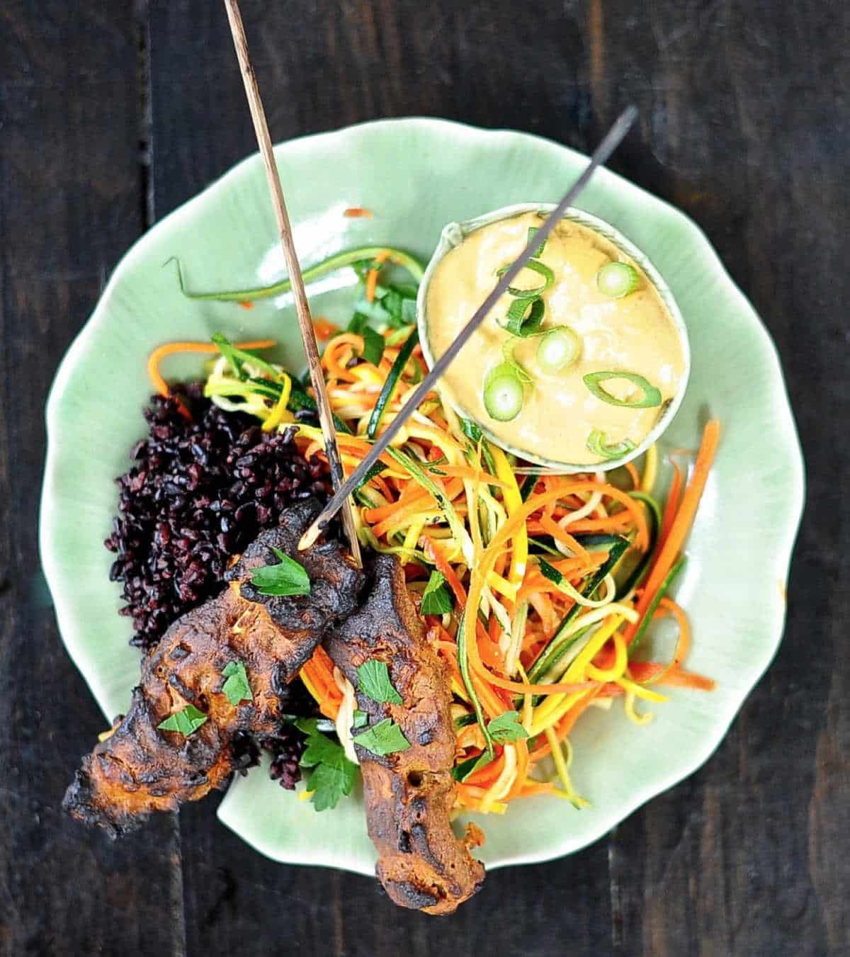 Vegan satay on a plate with peanut sauce in a small bowl.