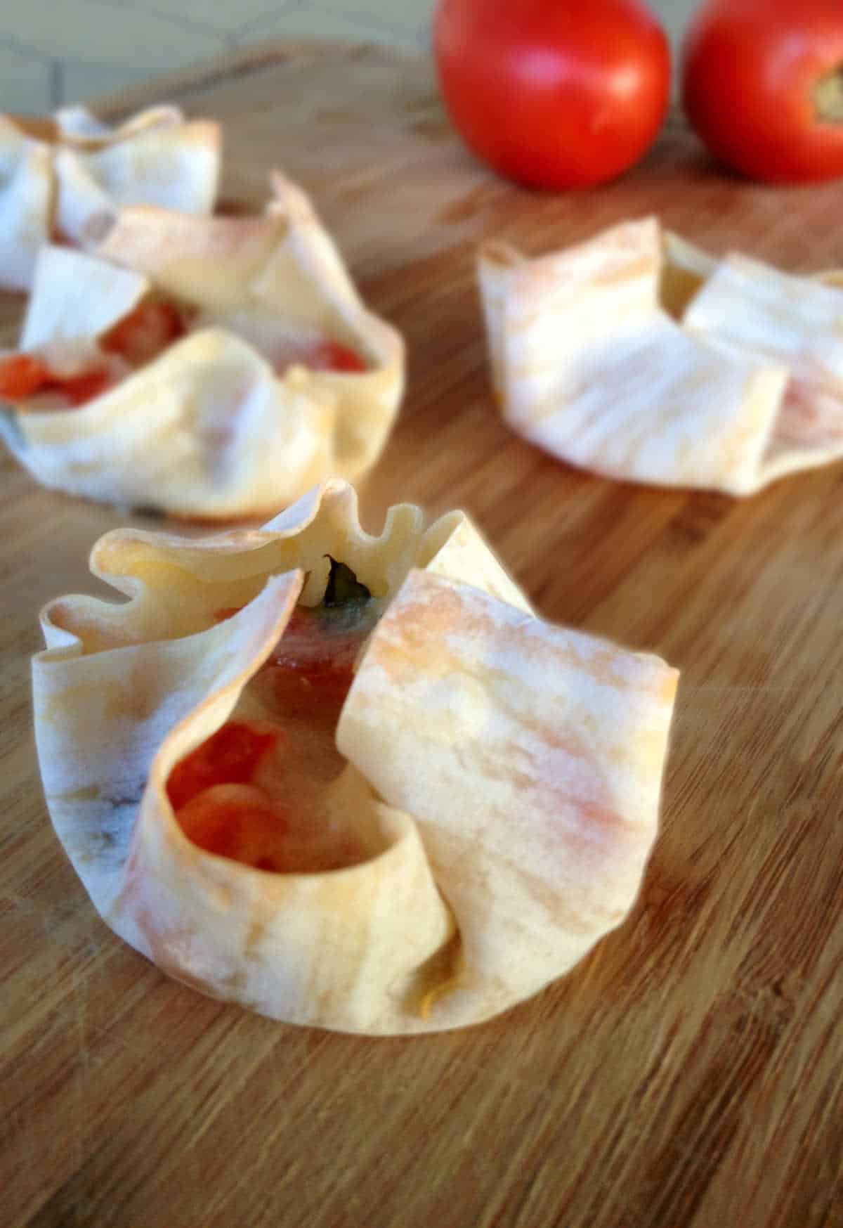 Wonton wrappers stuffed with vegan cheese and tomatoes on a cutting board.