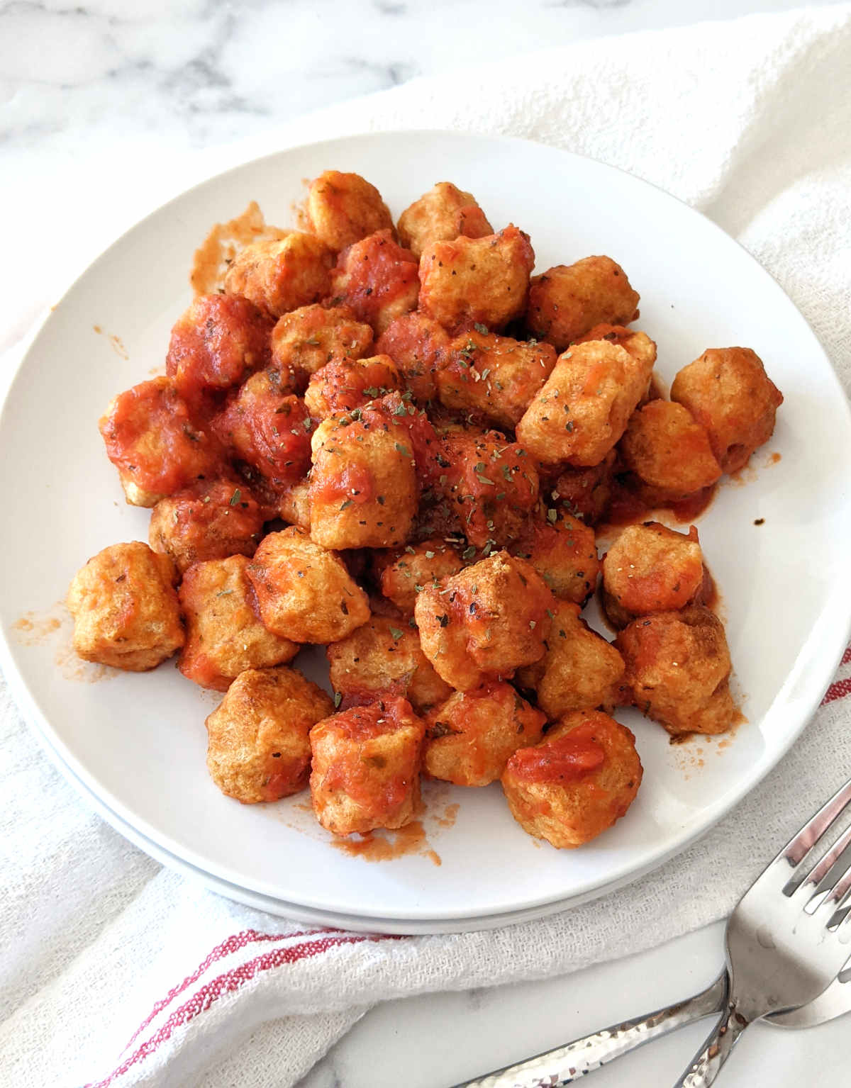 Air fried gnocchi served in a marinara sauce on a plate.