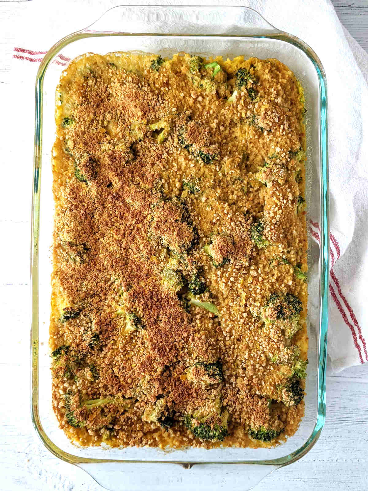 Baked cheesy vegan broccoli rice casserole in a large dish with a dish towel beside it.