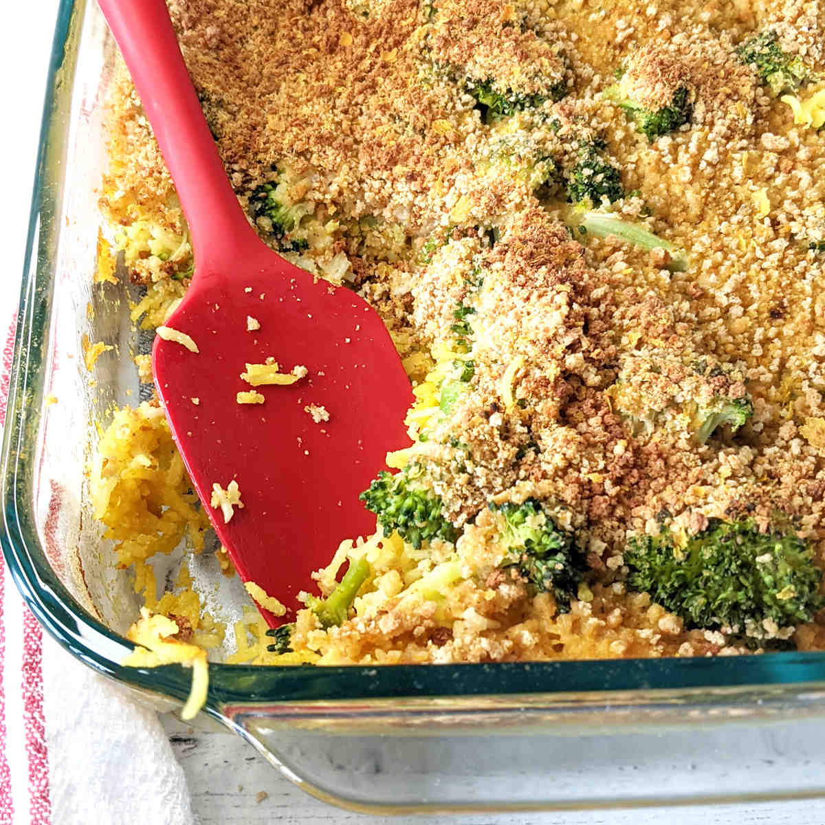 A casserole dish with cheesy vegan broccoli rice with a spatula resting in it.