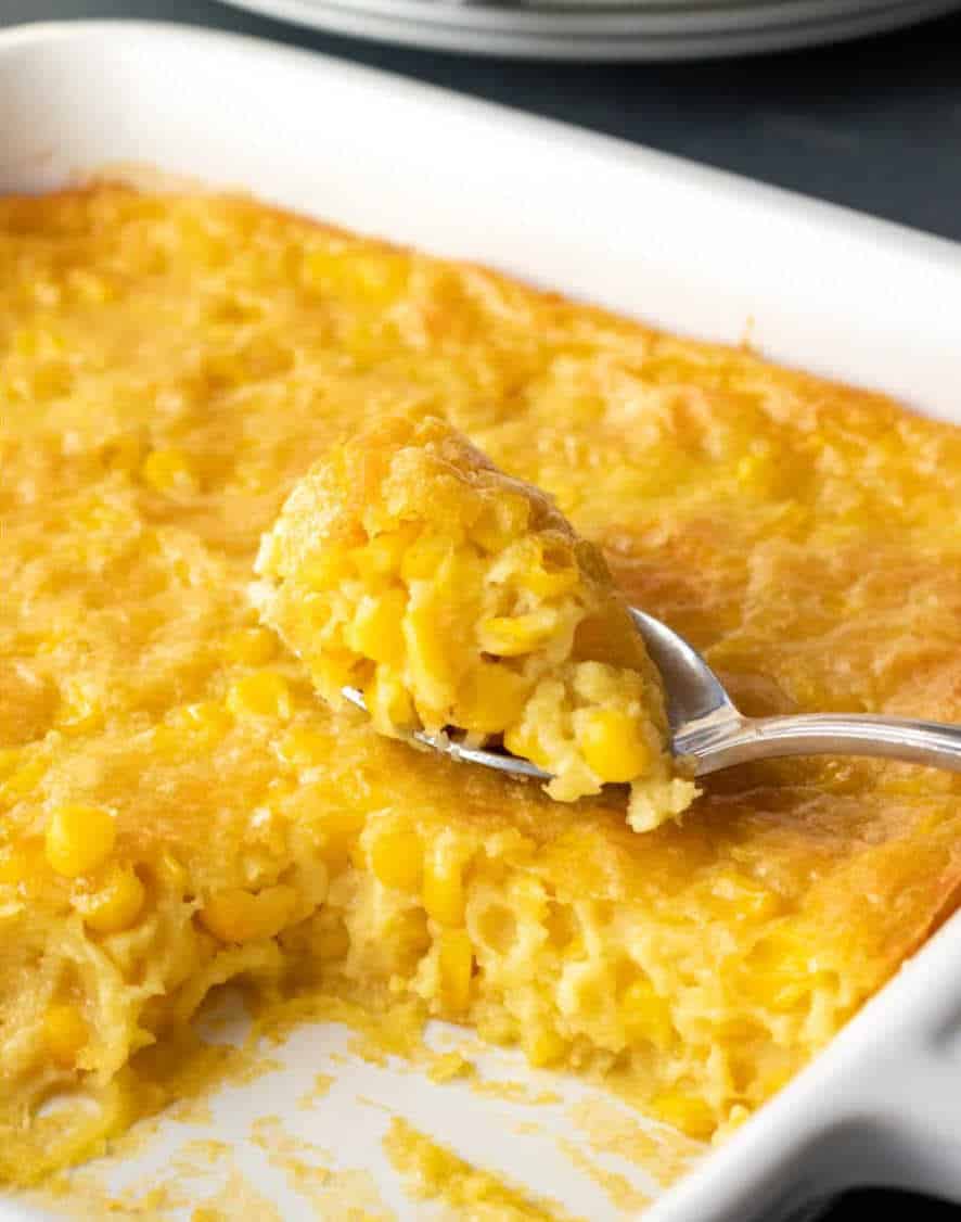 Corn pudding in a baking dish with a spoon resting on top holding a bite of it.