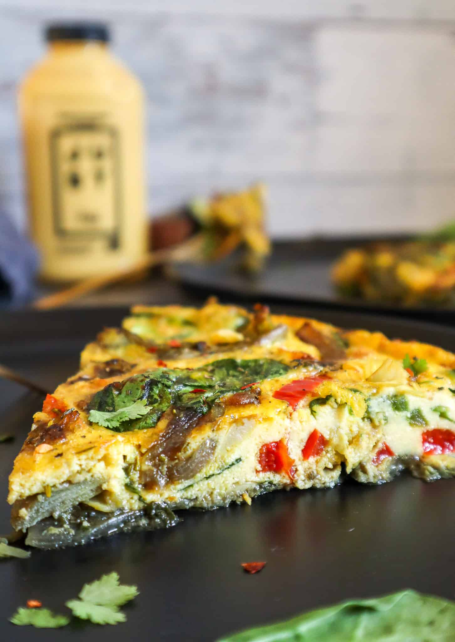 Slice of vegan frittata on a plate with a bottle of Just Egg in the background.
