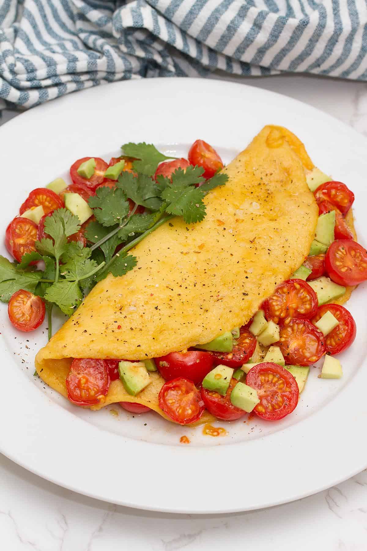 Just egg omelette with tomatoes, avocado and cilantro on a plate.