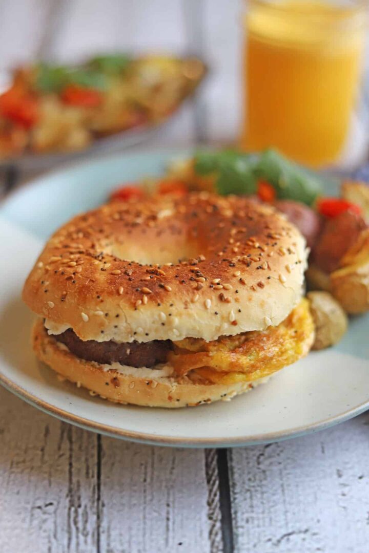 Vegan bagel breakfast sandwich on a plate stuffed with Just Egg and vegan sausage.