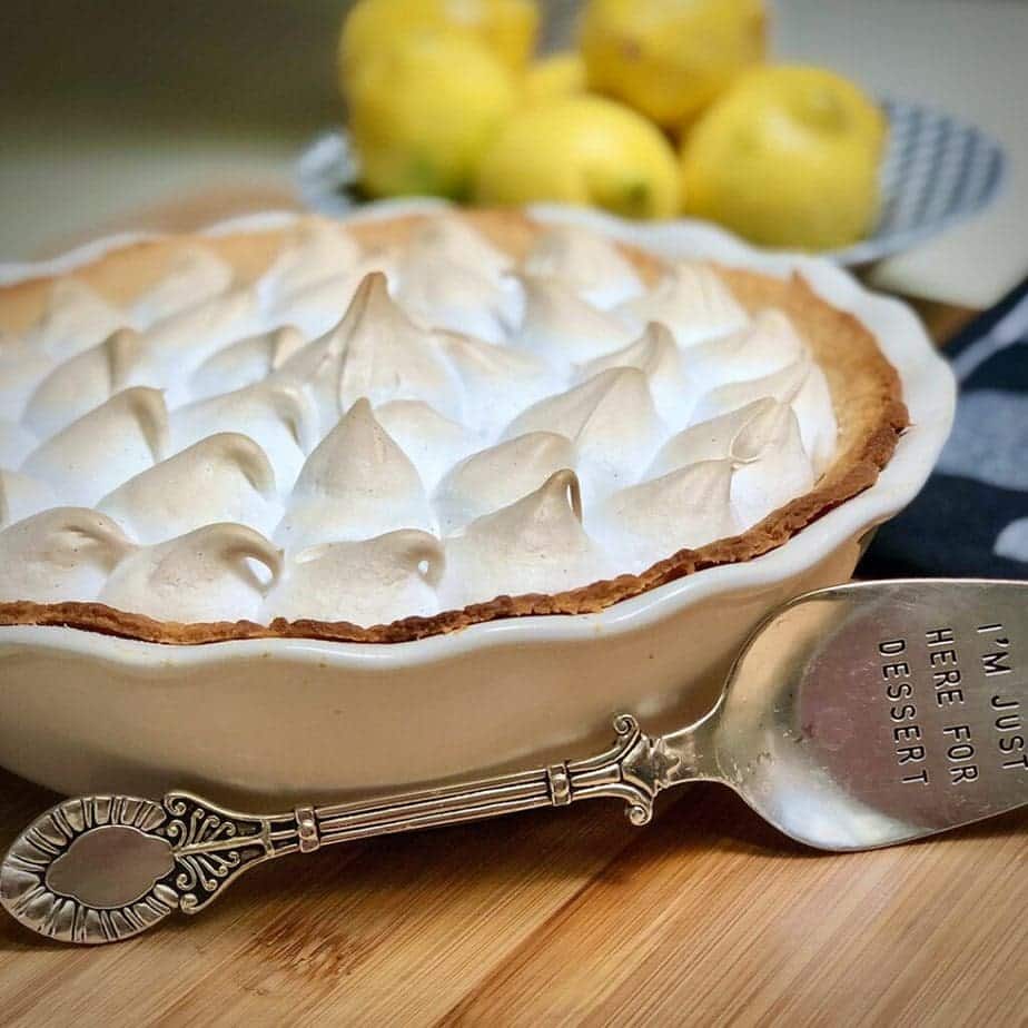 Vegan lemon meringue in a pie dish next to a serving spatula.