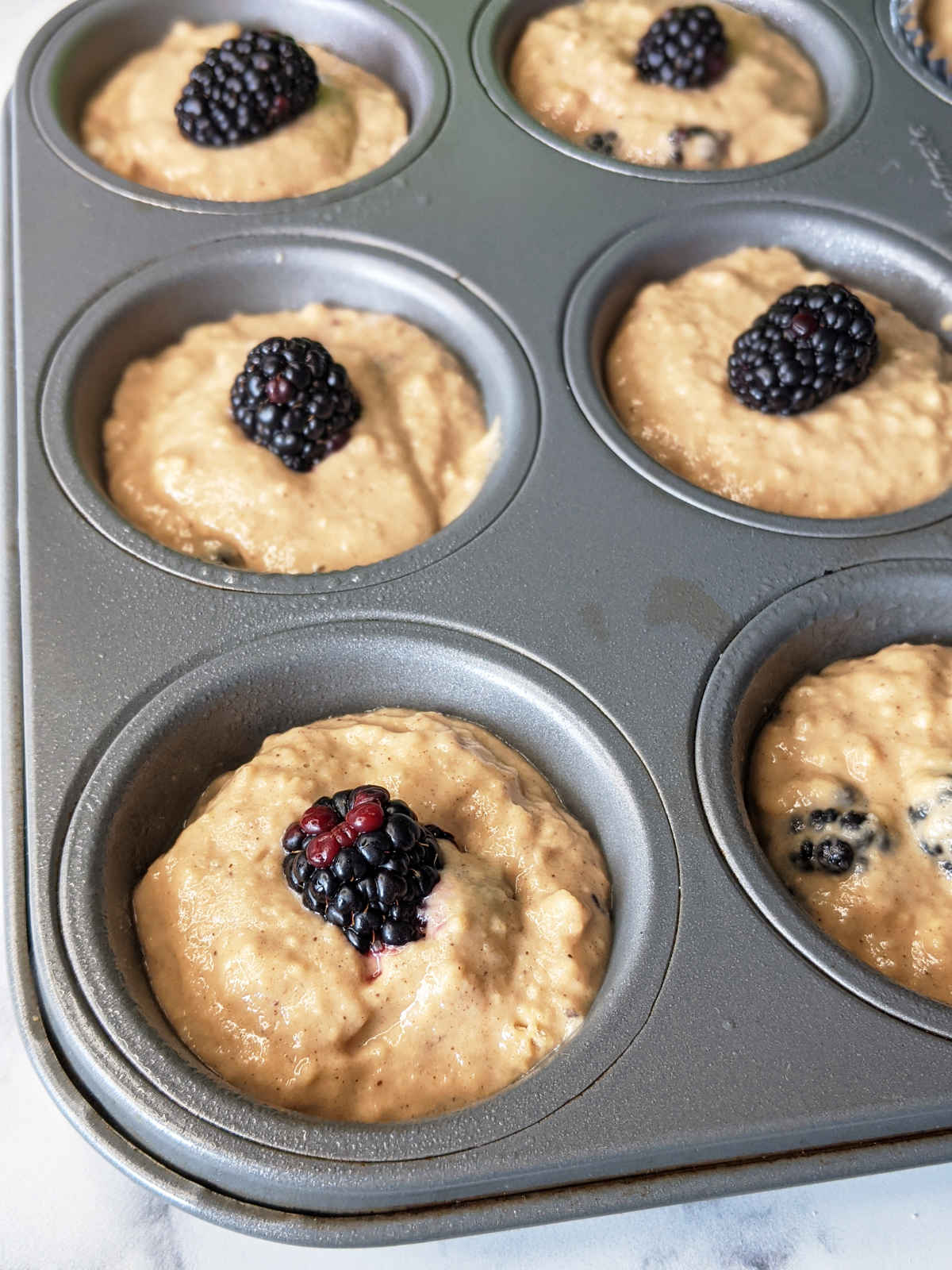 Prepared vegan blackberry muffins in pan before baking, topped with fresh blackberries.