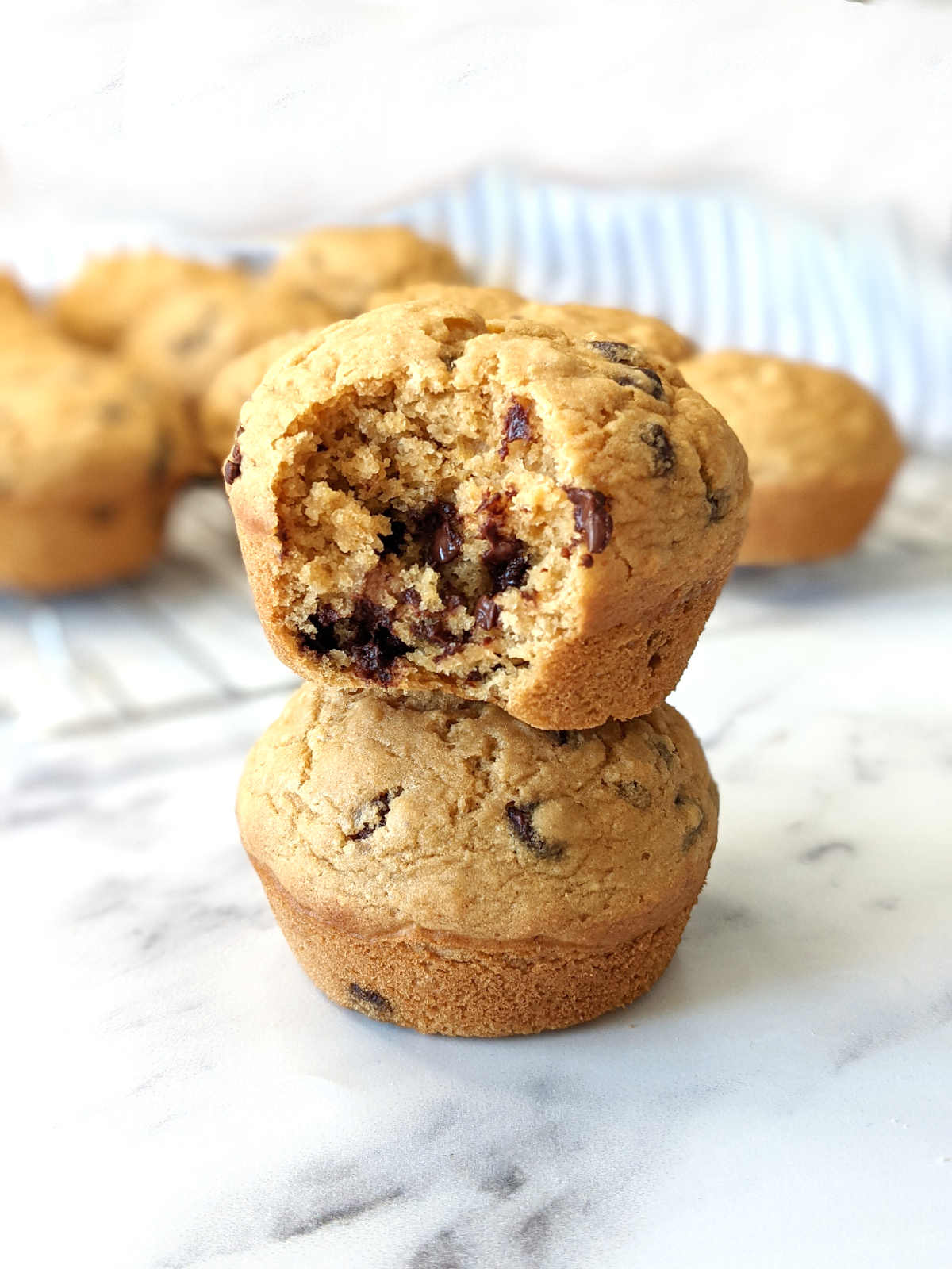 One vegan chocolate chip muffin with a bite missing sitting on top of another muffin.