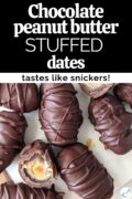 Dates stuffed with peanut butter and covered with chocolate sitting on a serving board with a couple dates cut in half, with text overlay "Chocolate peanut butter stuffed dates, tastes like snickers!".