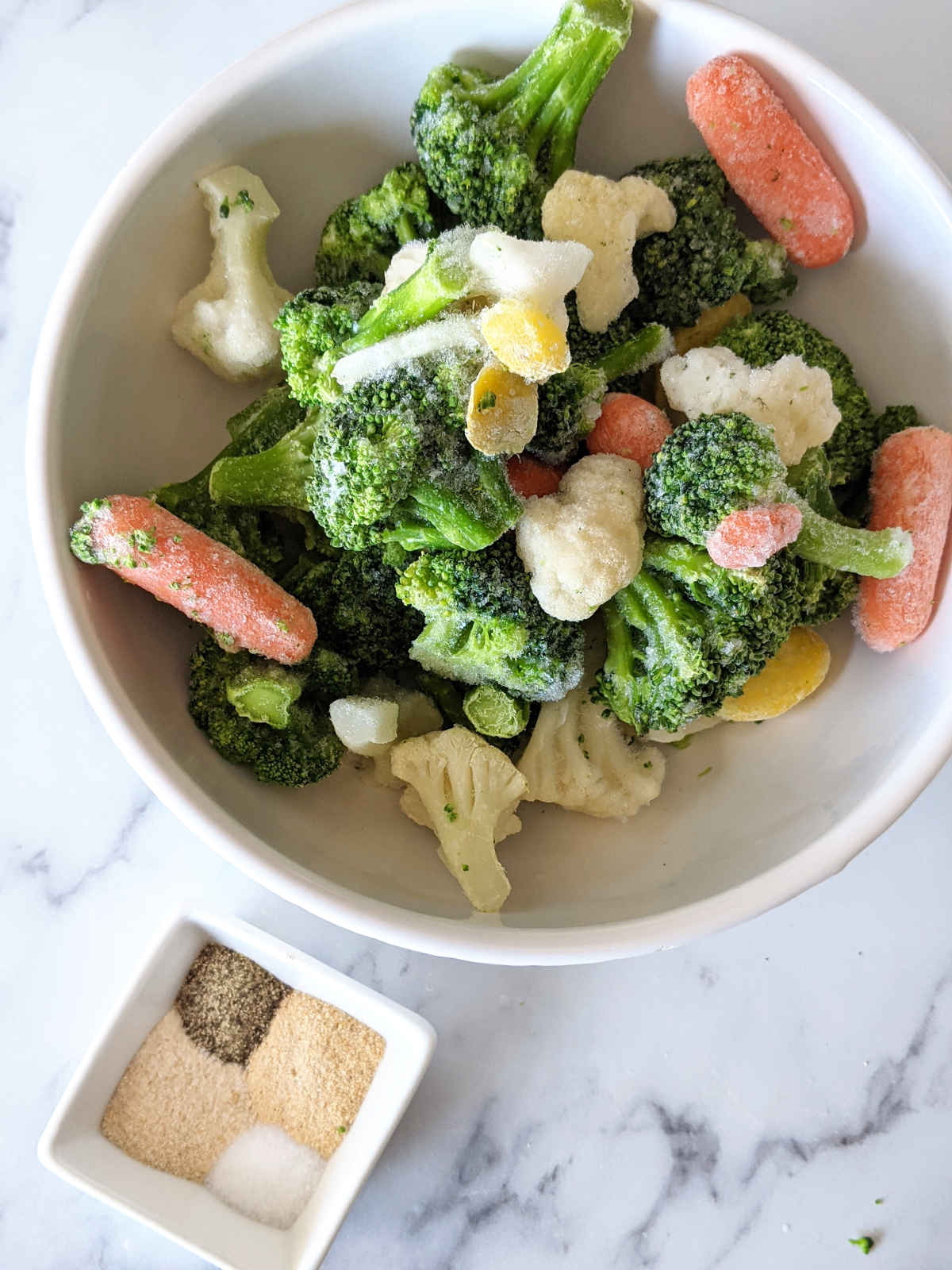 Frozen vegetables in a bowl next to a small dish holding measured seasonings.