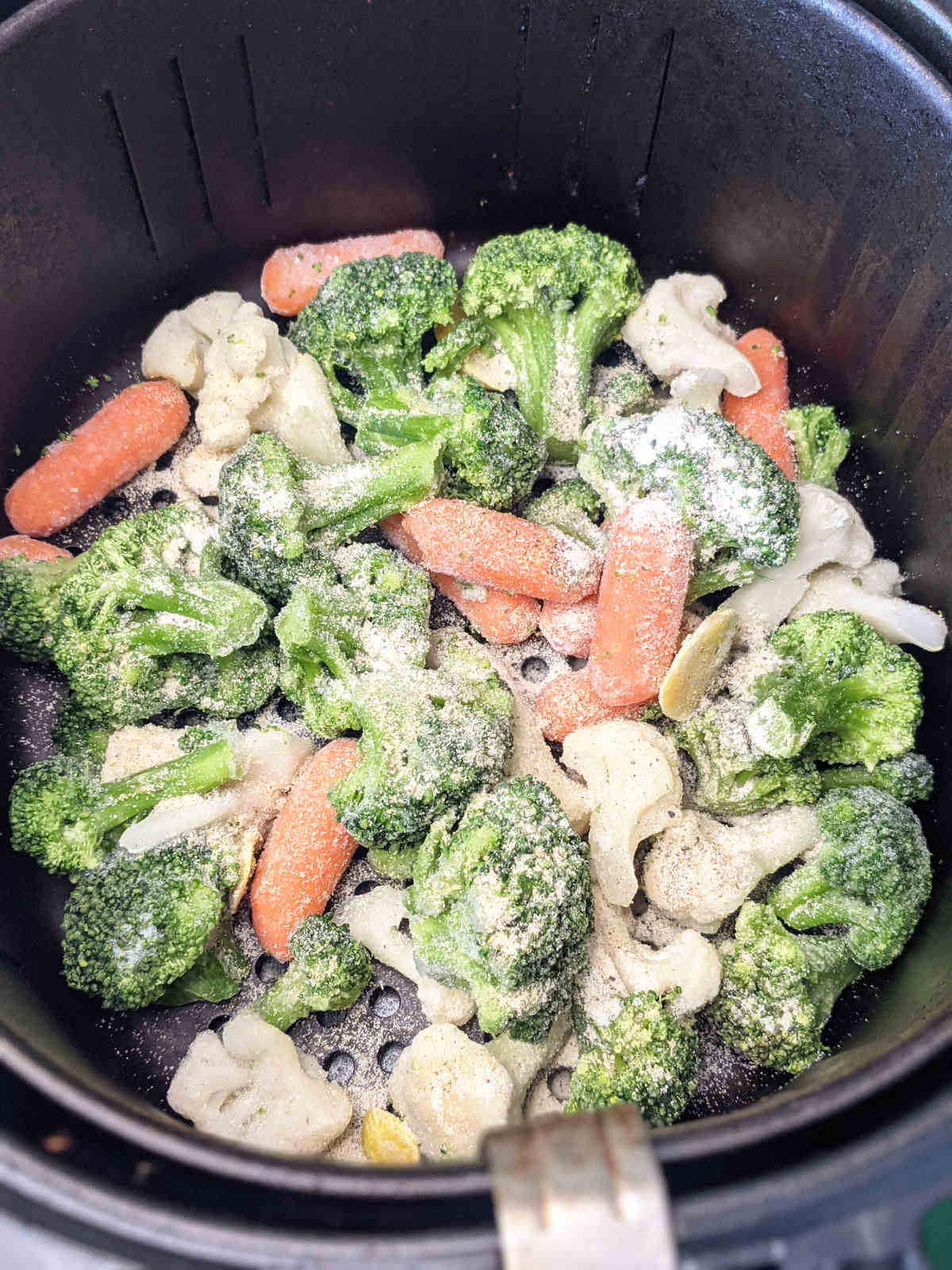 Frozen veggies in air fryer topped with seasonings.