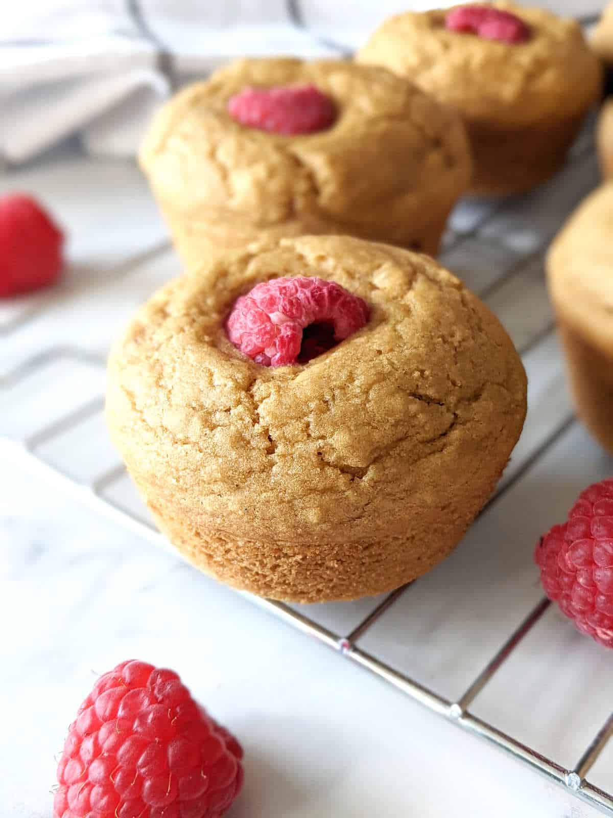 Vegan muffin topped with a raspberry sitting on a cooling rack.