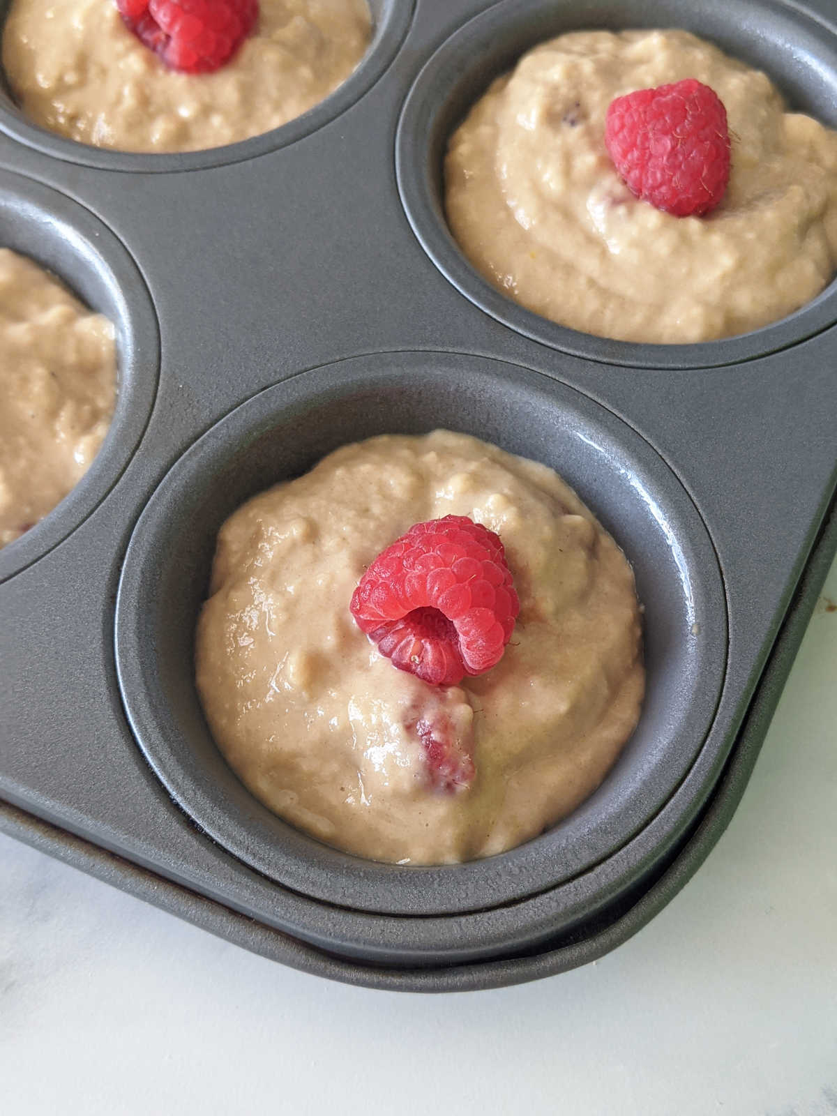 Vegan raspberry muffin batter in a muffin pan topped with a fresh raspberry.