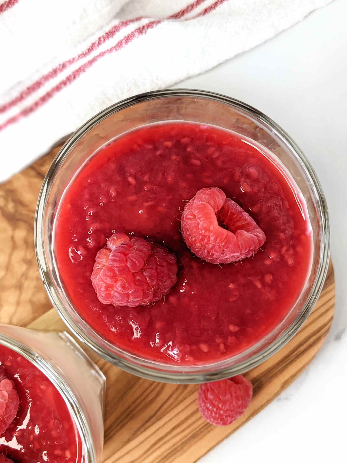 Raspberry sauce covered cheesecake in a glass with more fresh raspberries on top.