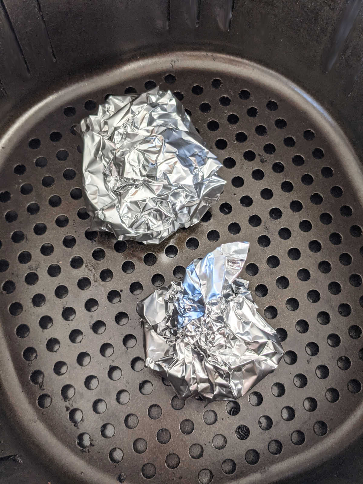 Garlic bulbs wrapped in foil and sitting in an air fryer basket.