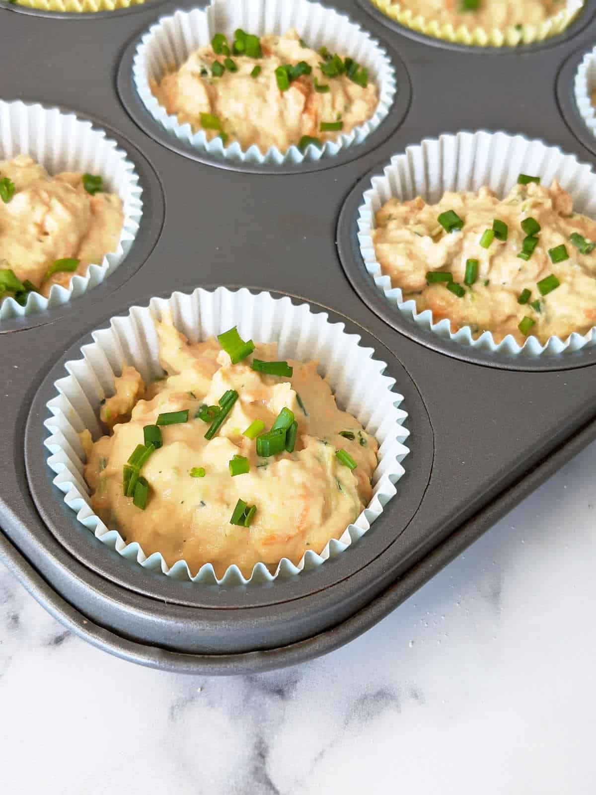 Savory muffin batter prepared in lined muffin pan topped with chives.