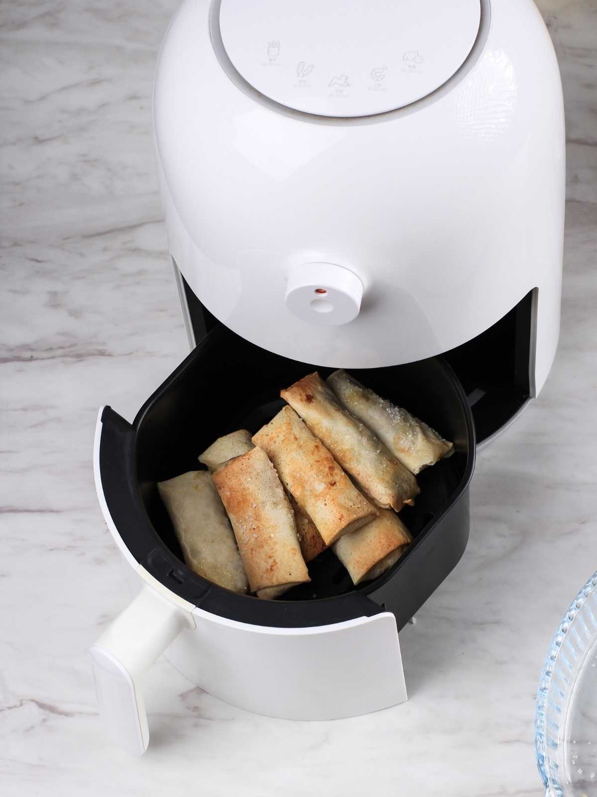 Air fryer open with spring rolls sitting in the basket.