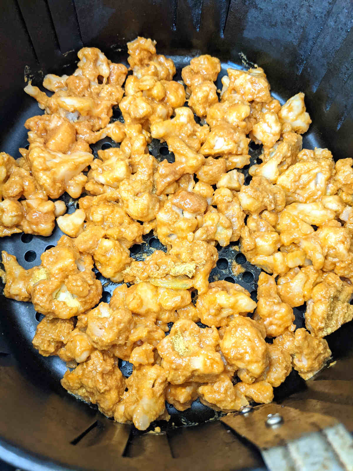 Coated frozen cauliflower in a single layer in an air fryer basket.