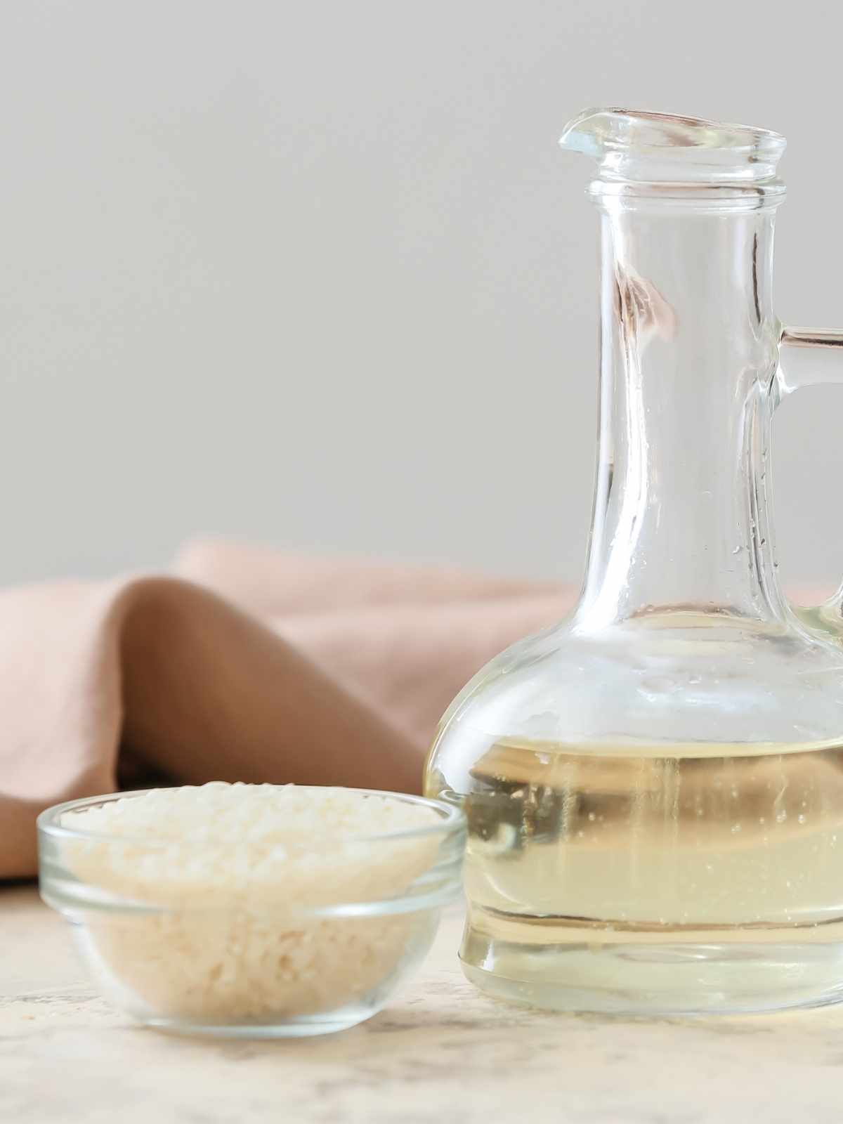 Glass bottle of white rice vinegar next to a small bowl of white rice.