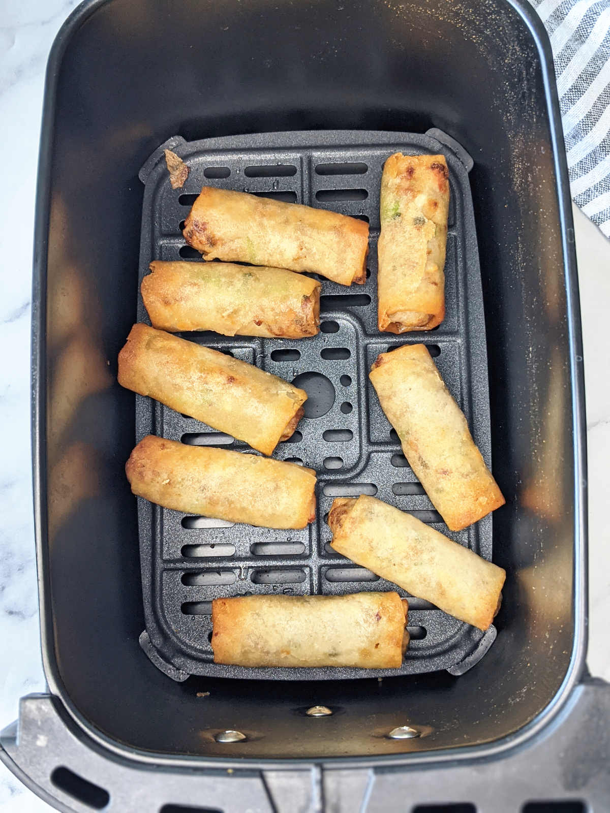 Frozen spring rolls in air fryer basket after cooking.