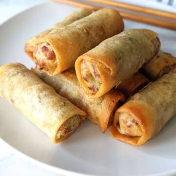 Air fryer frozen spring rolls stacked on a plate.