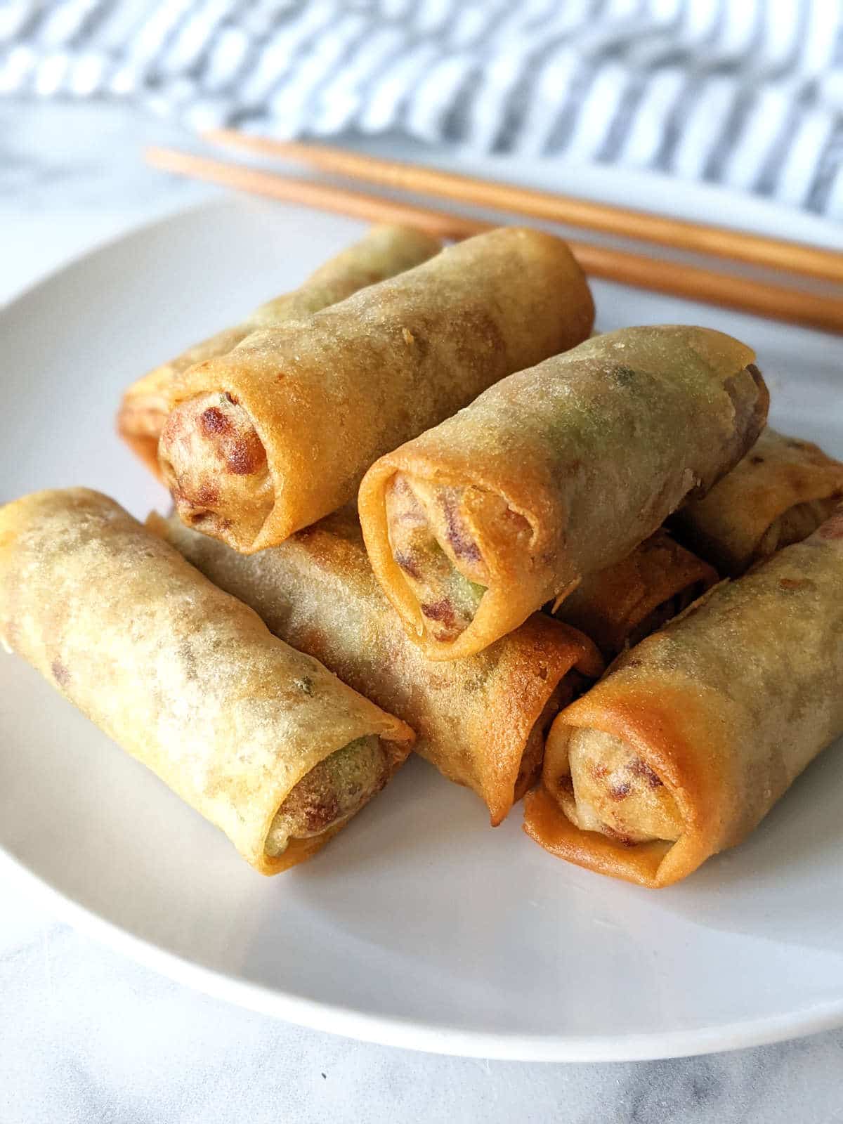 Air fryer frozen spring rolls stacked on a plate.