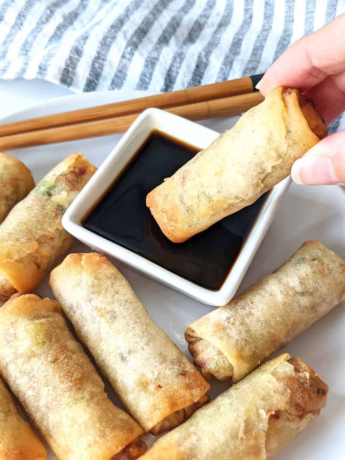 Hand holding a spring roll and dipping it into some soy sauce.