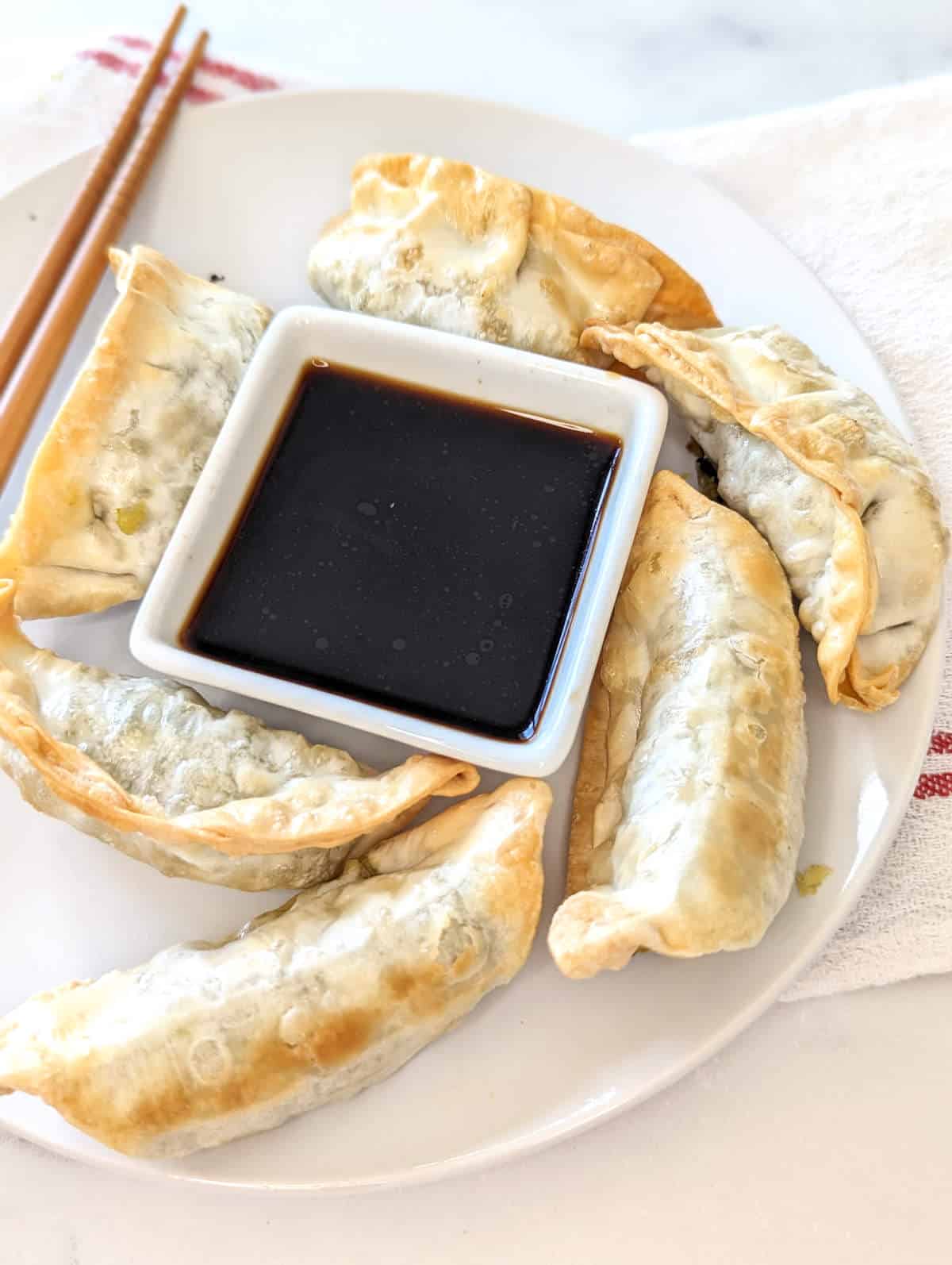 Cooked potstickers on a plate with a side of soy sauce.