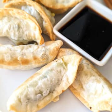 Cooked potstickers on a plate with a side of soy sauce.