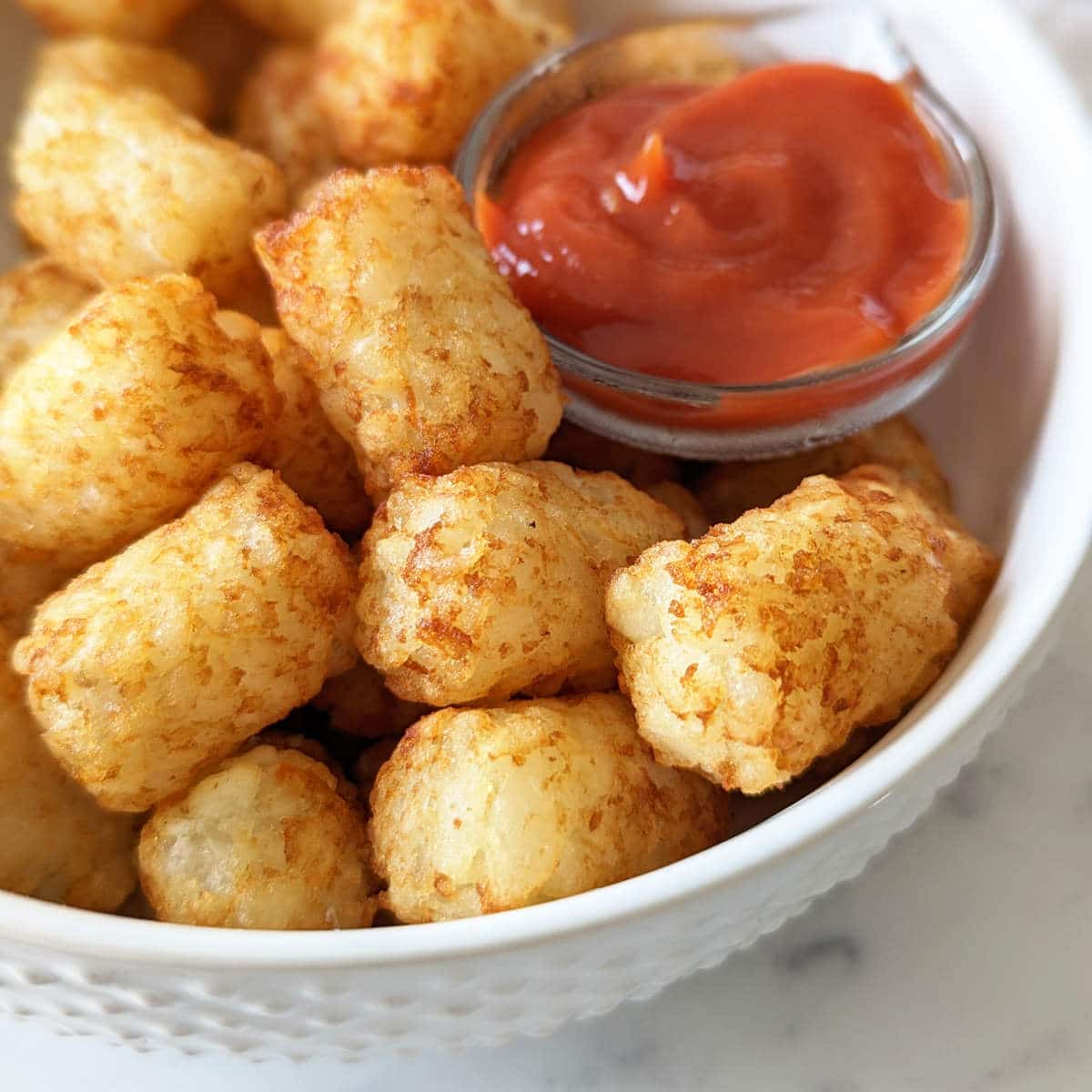 Golden air fried tater tots in a bowl with a side of ketchup.