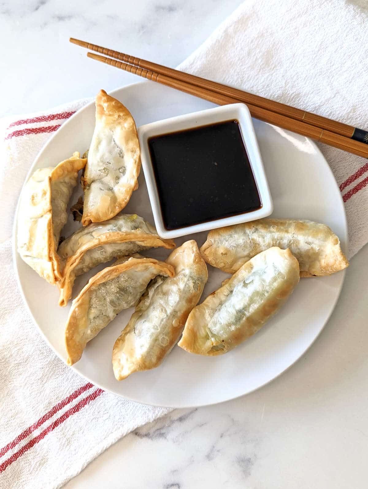 Air fryer frozen potstickers on a plate with chopsticks and a small bowl of soy sauce.