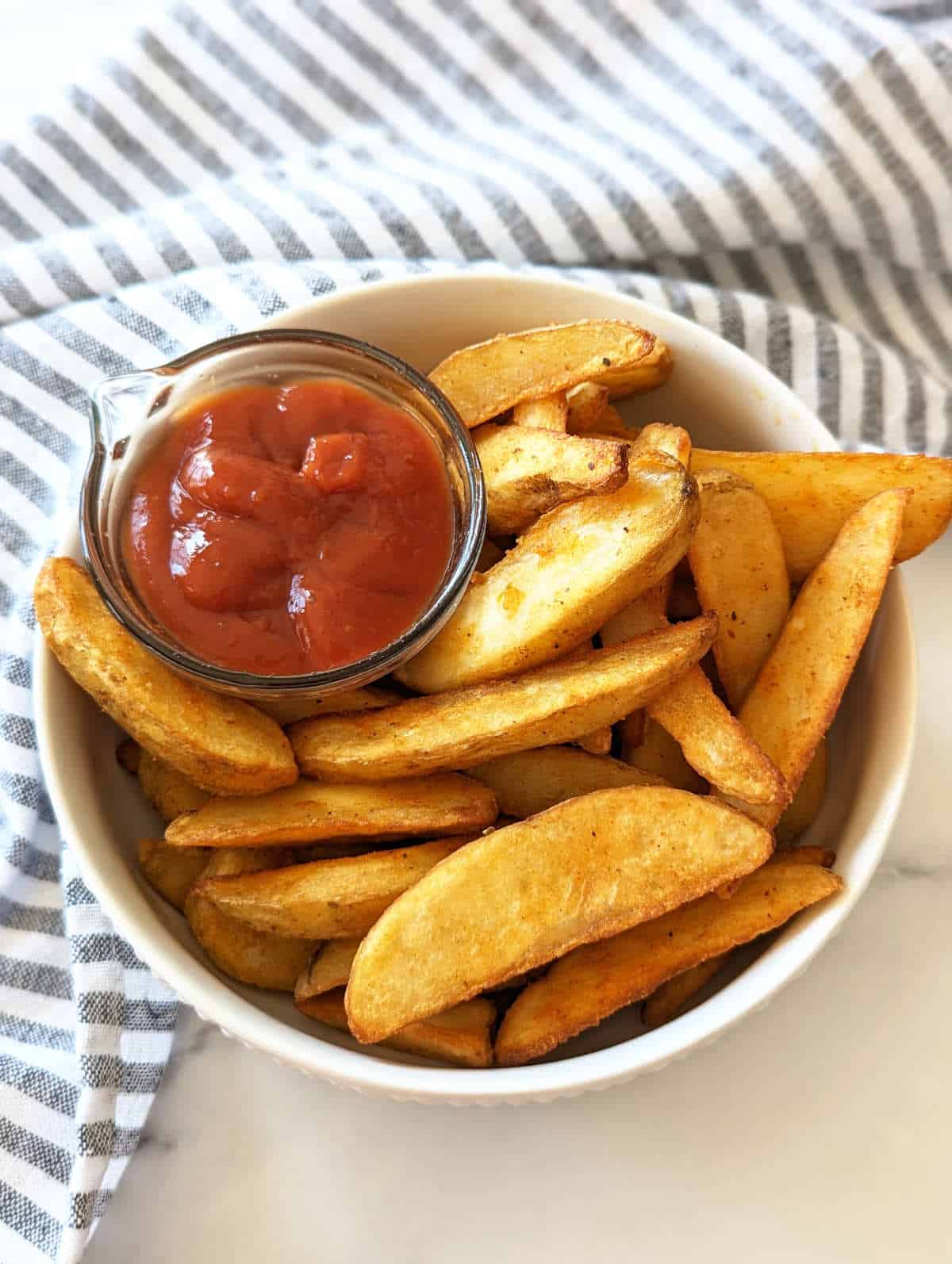 Cooked air fryer frozen potato wedges in a bowl served with ketchup.