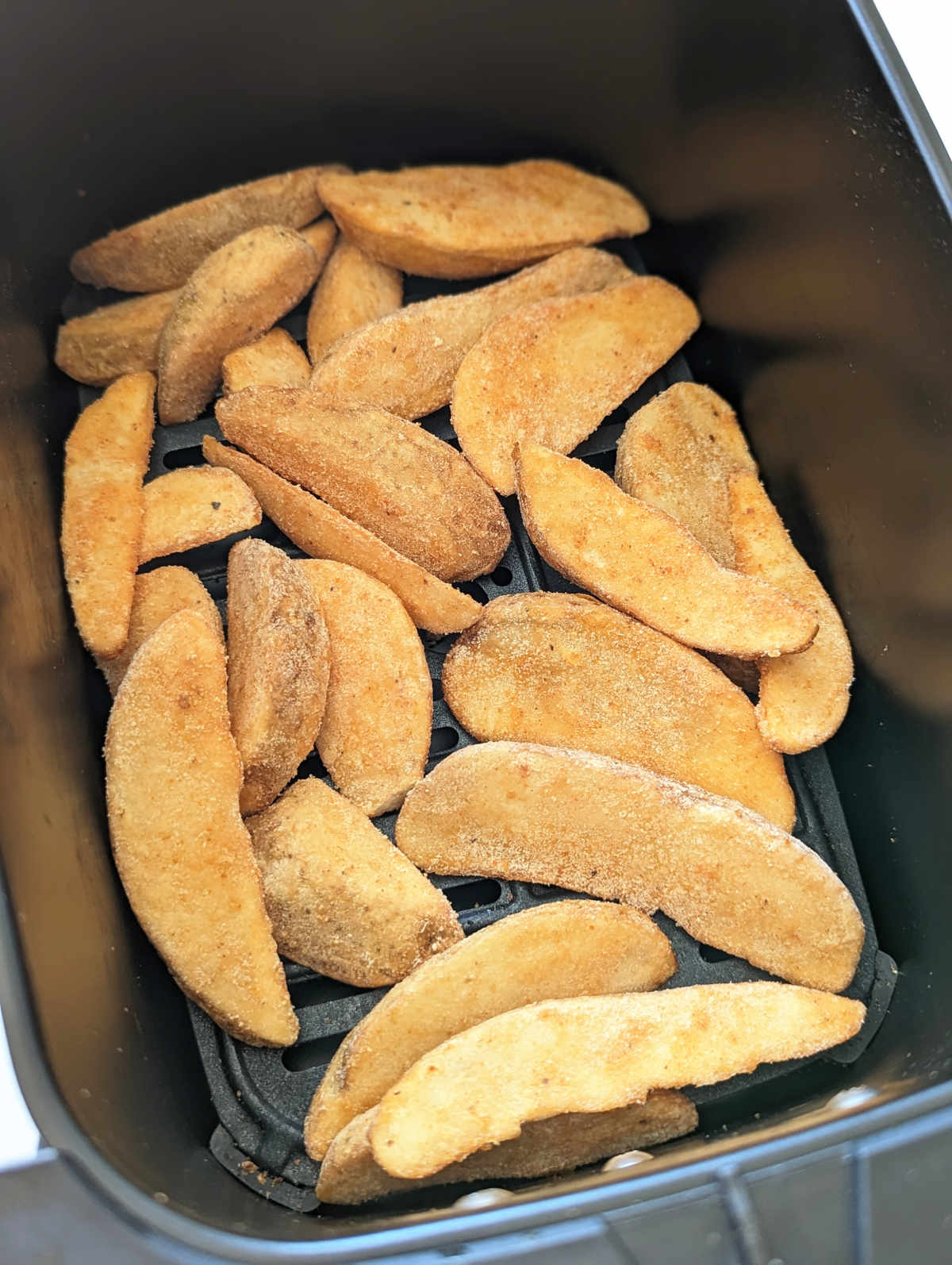 Frozen potato wedges in an air fryer basket.