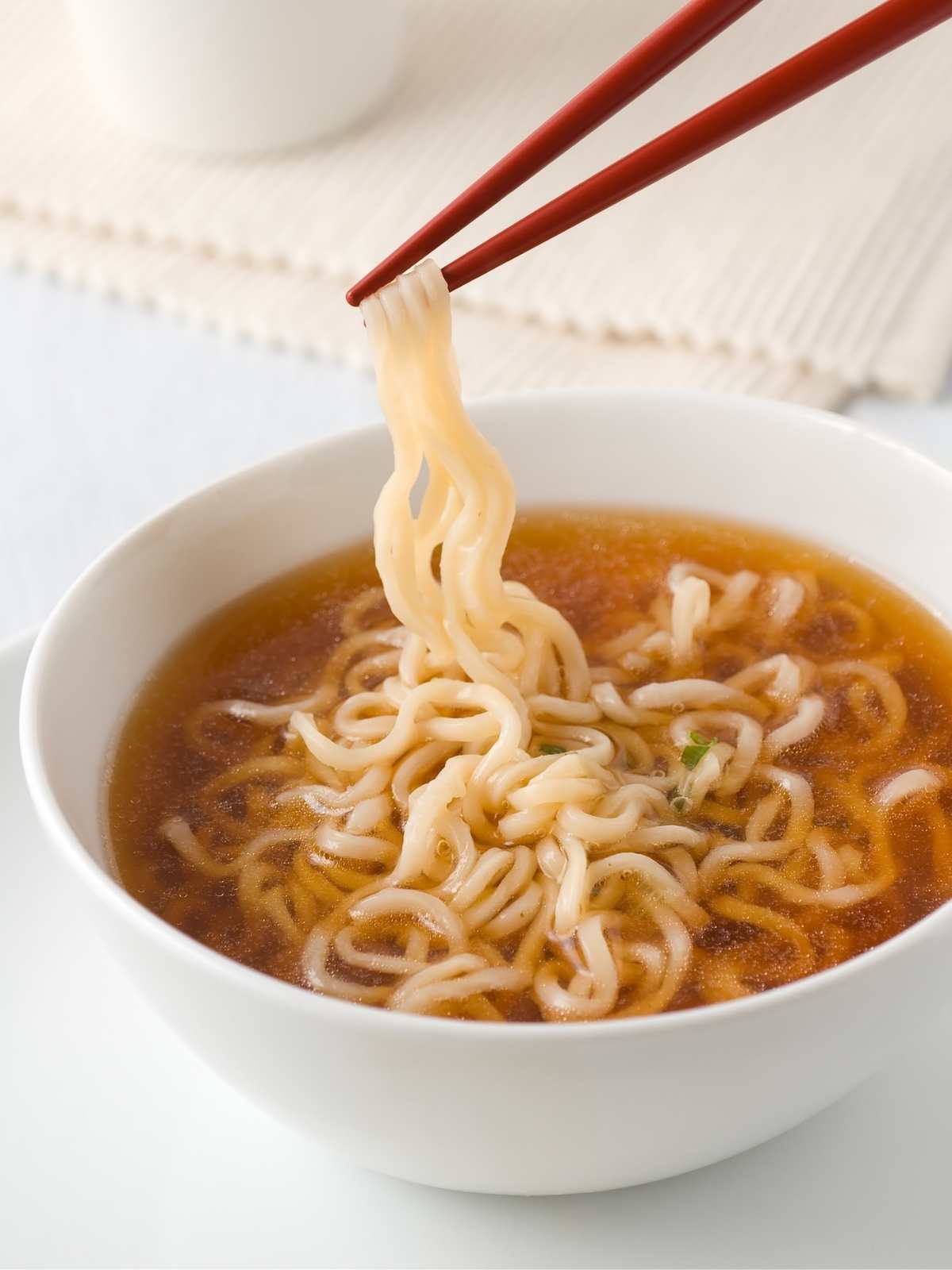White bowl of ramen noodles with chopsticks holding a bit of noodles.